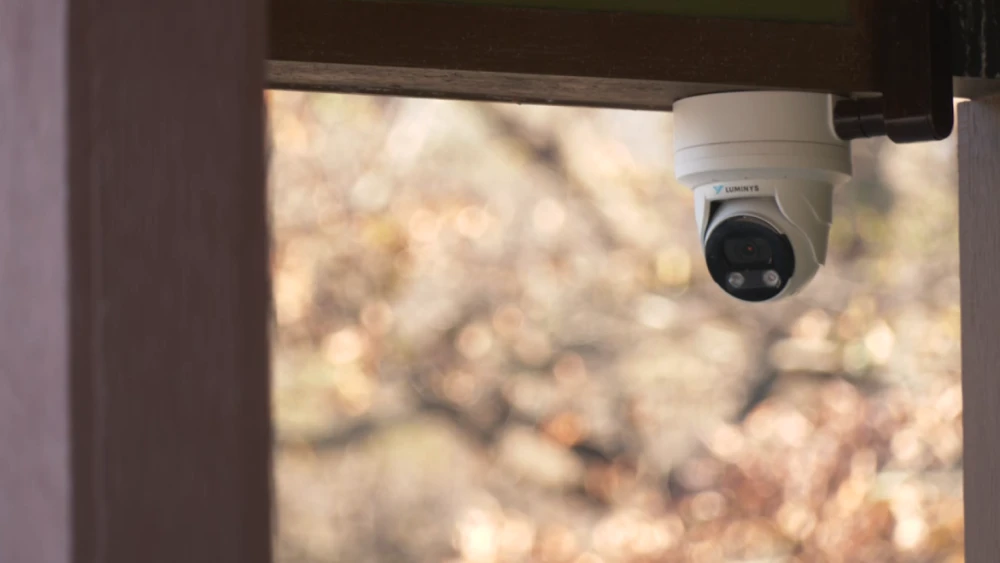 A small white camera with a large black lens hangs from the roof of an outdoor pavilion.