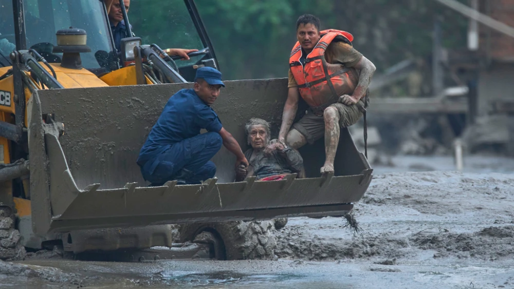 Rescuers use an earthmover to carry a victim of flash flooding to safety along the Trishuli River in Nepal
