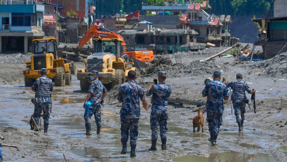 Nepalese policemen watch as earthmovers clear the debris of flash flooding in Nepal